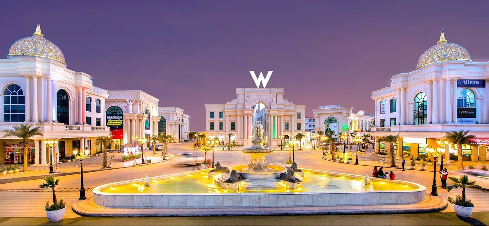 Illuminated grand classical fountain plaza with neoclassical domed architecture and retail boulevard at Omaxe